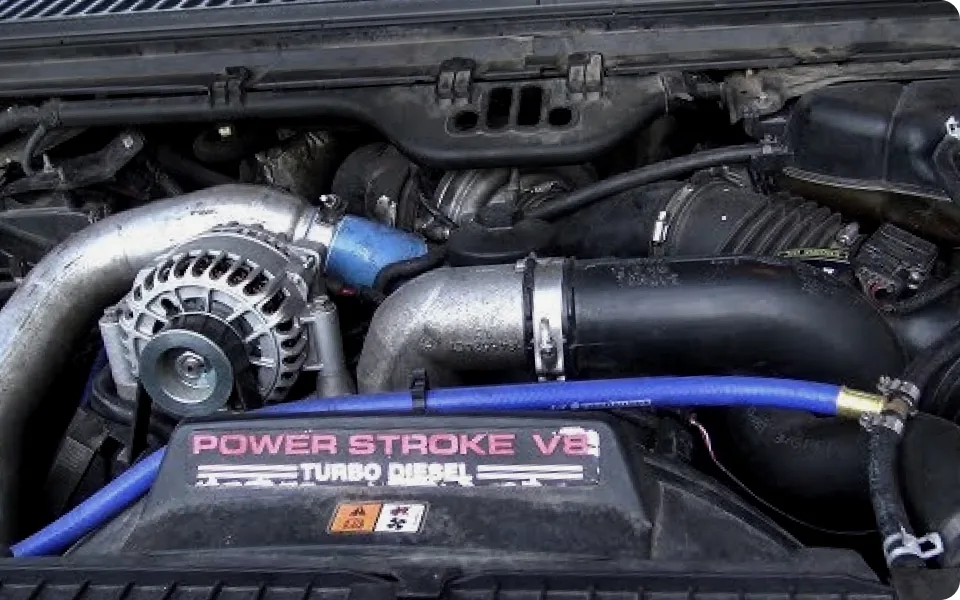 A close-up view of a Ford Power Stroke V8 Turbo Diesel engine compartment, showcasing various hoses, belts, the alternator, and the engine cover with the "Power Stroke V8 Turbo Diesel" branding.