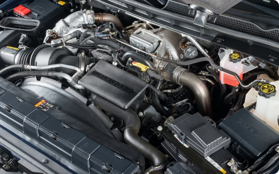 A detailed overhead view of a truck engine compartment, showcasing various mechanical and electrical components, including hoses, belts, fluid reservoirs, and wiring harnesses. The engine appears complex and modern.